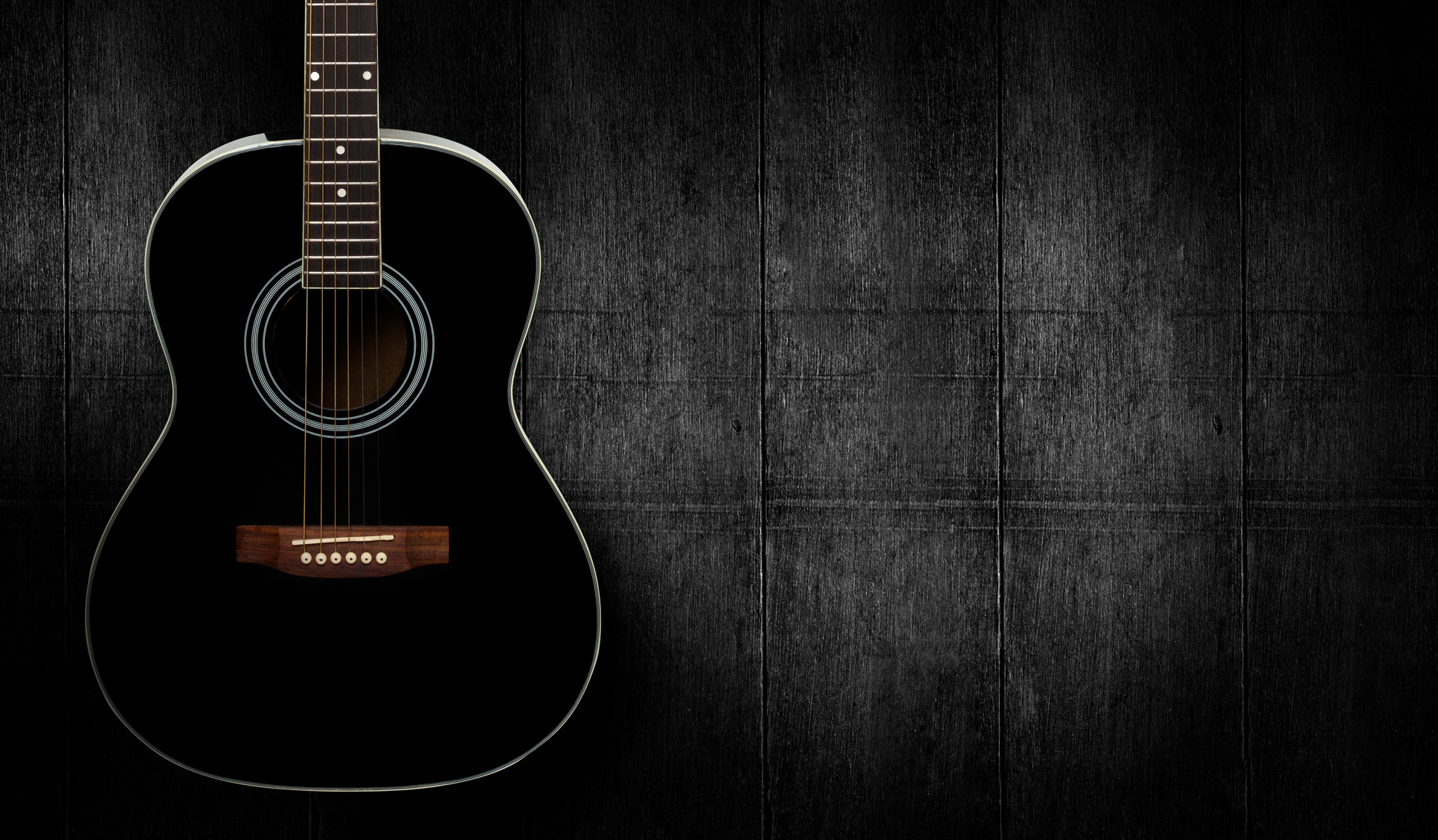 Black acoustic guitar on dark black wooden background.